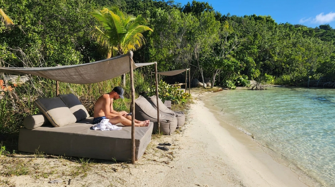 A man sitting quietly on a daybed under palm trees, head bowed over his notebook — the slower, inward-turning path.